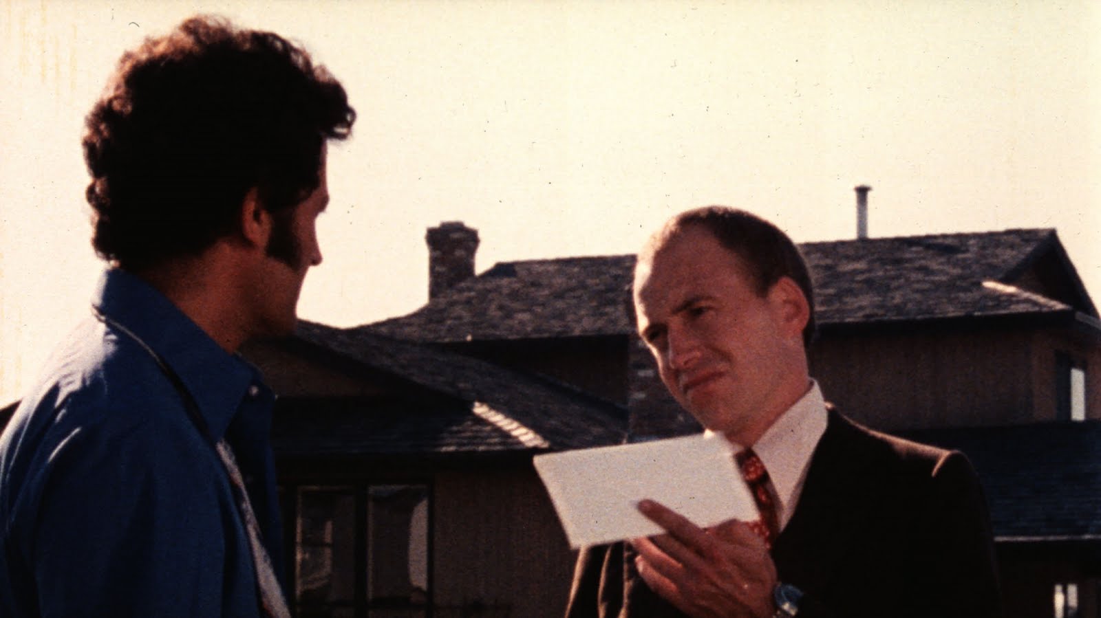 A still from Skip Tracer: a man holds out an envelope to another man.