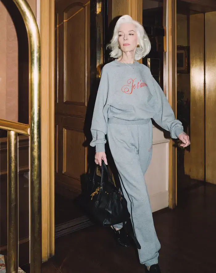 A woman walks through a door while wearing matching grey pants and sweater.