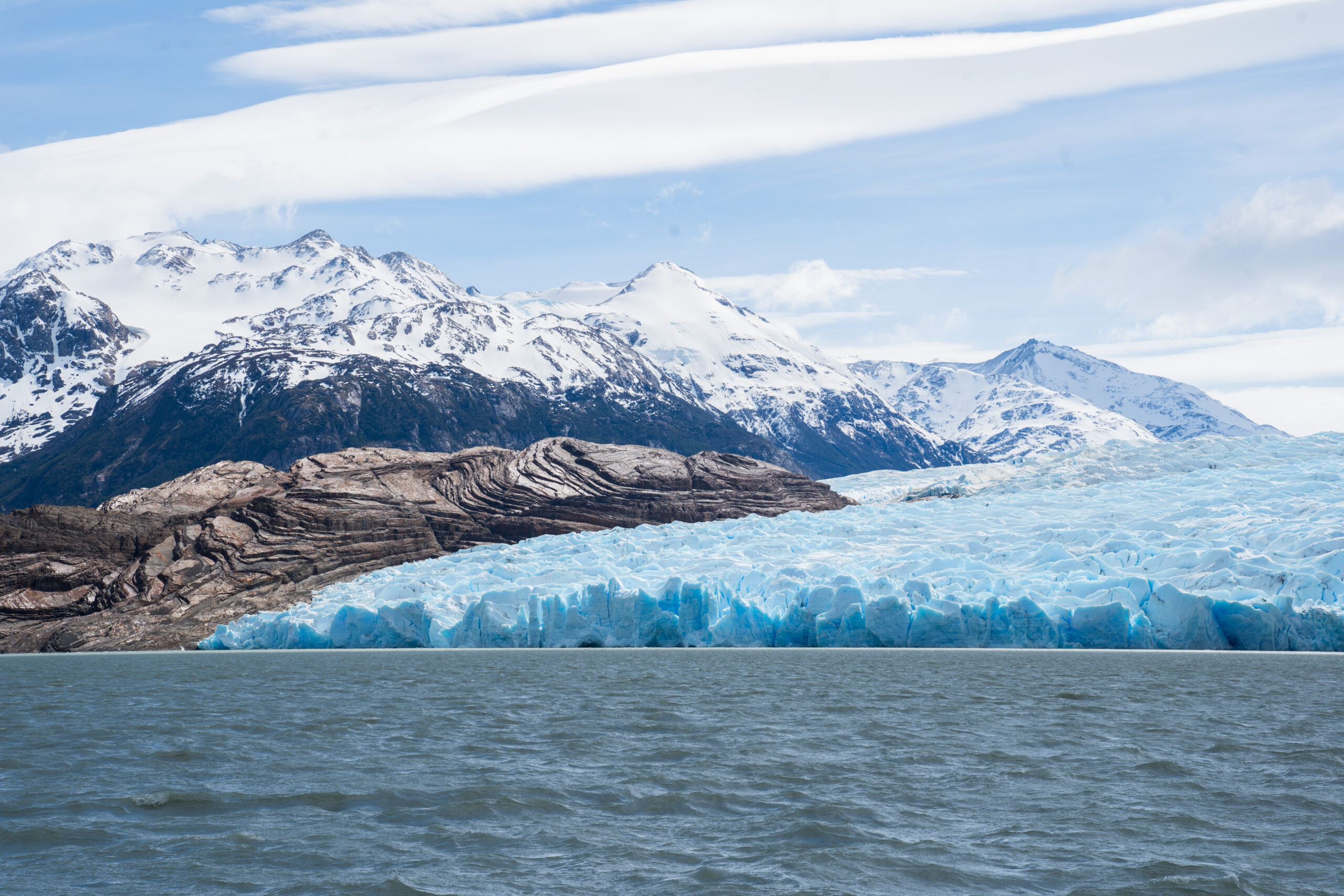 A glacier on a river bank in front of a mountain range.